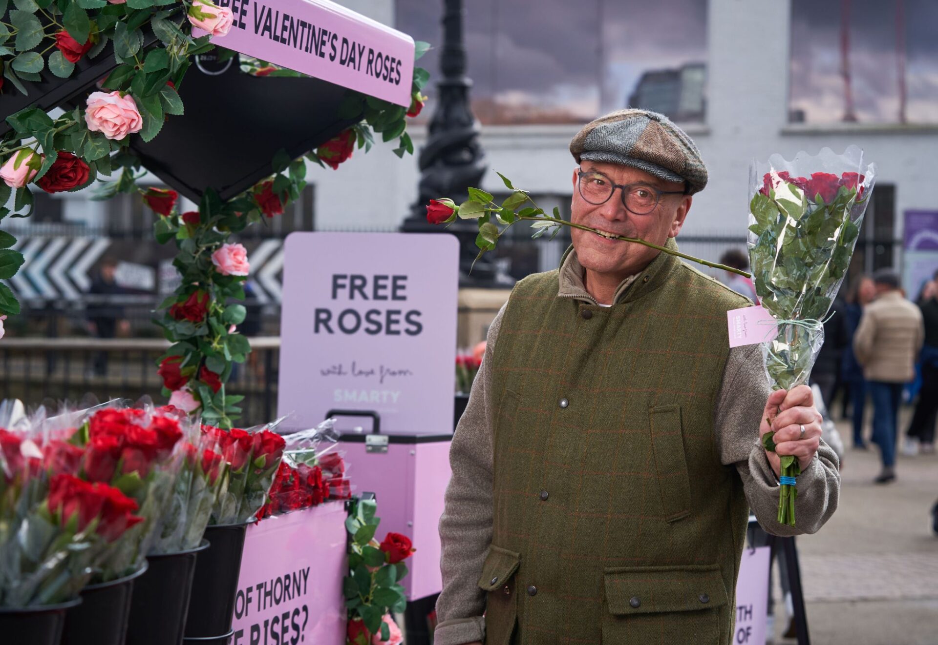 Gregg Wallace, a white man wearing hat and coat holding a bunch of red roses to give to people for free on the streets of London. 