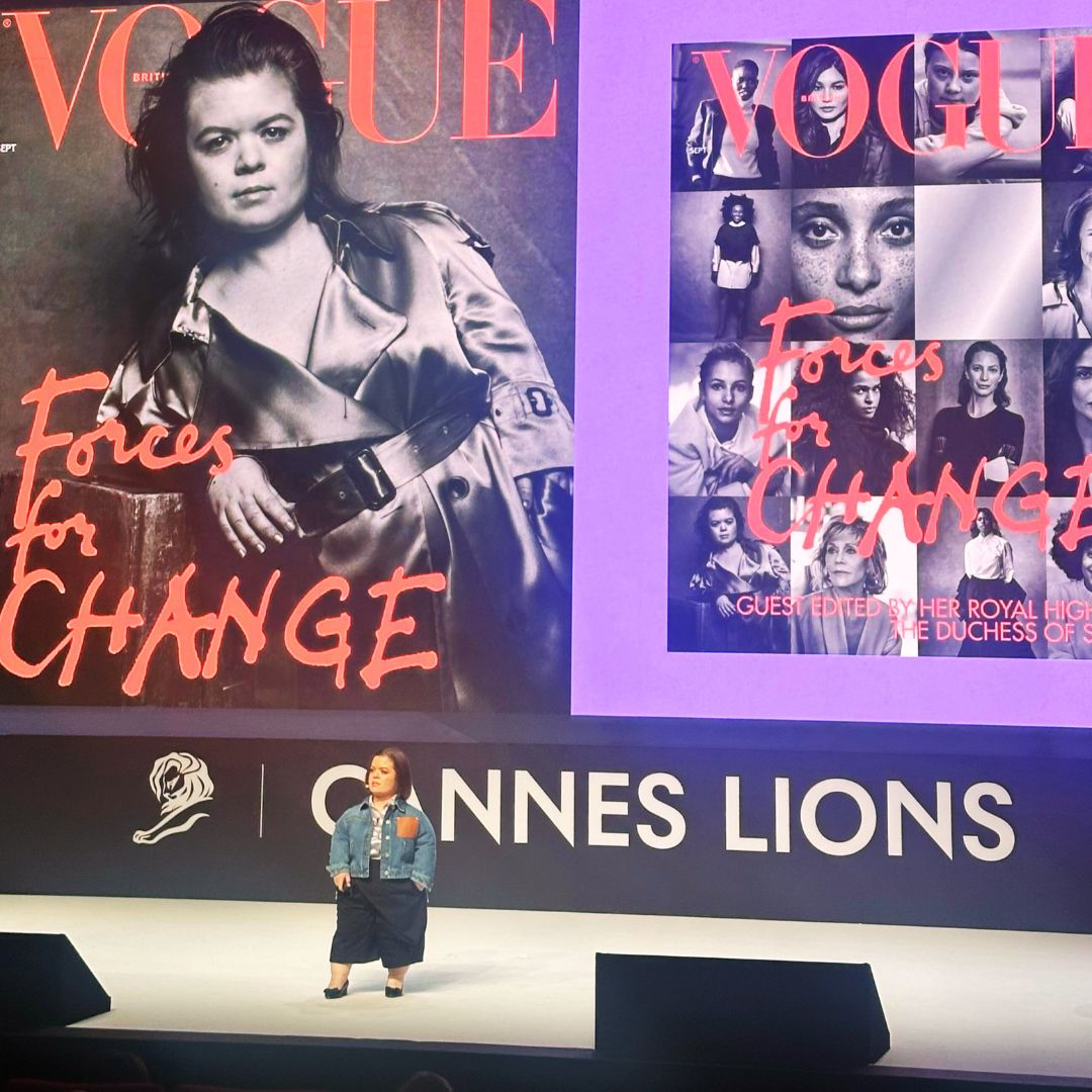 One person on stage with big screen behind them showing them on the cover of Vogue Magazine