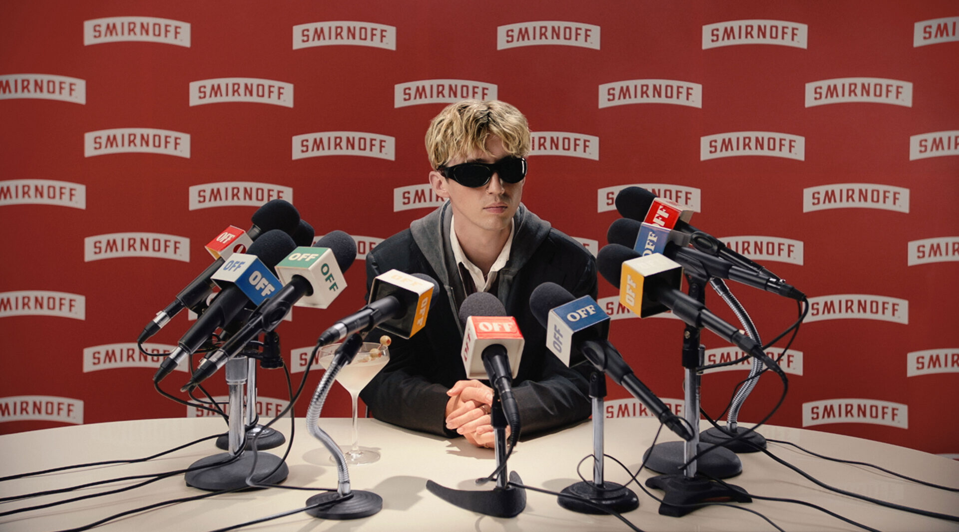 Troye Sivan sitting at media table with microphones from news outlets in front.